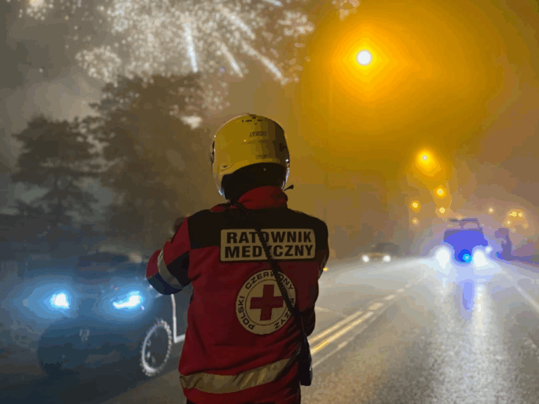 Ratownik medyczny PCK Koszalin podczas zabezpieczenia medycznego pokazu fajerwerków, w tle karetka i quad ratowniczy