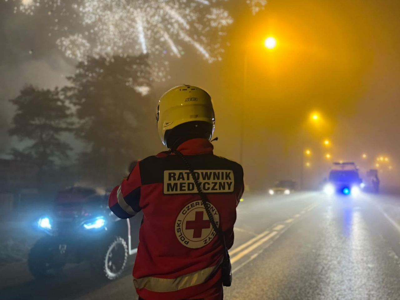 Ratownik medyczny PCK Koszalin podczas zabezpieczenia medycznego pokazu fajerwerków, w tle karetka i quad ratowniczy